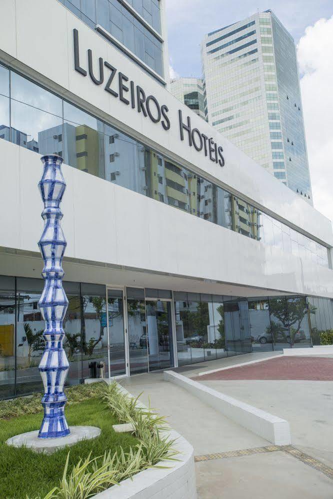 Hotel Luzeiros Recife Kültér fotó The photo shows a modern hotel building with large glass windows and a sleek, white facade. In front of the hotel, there is a tall, decorative sculpture that features a unique, twisting shape with a blue and white color scheme. The hotel name is prom